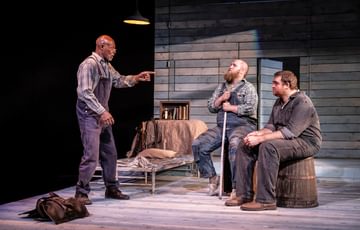 Jeff Alexander who plays crooks is stood up pointing at Ben Wilson, who plays Candy, and William Young, who plays Lennie.