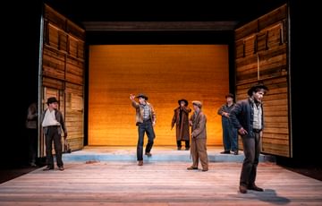 The actors are stood around the stage and one of them explains something.