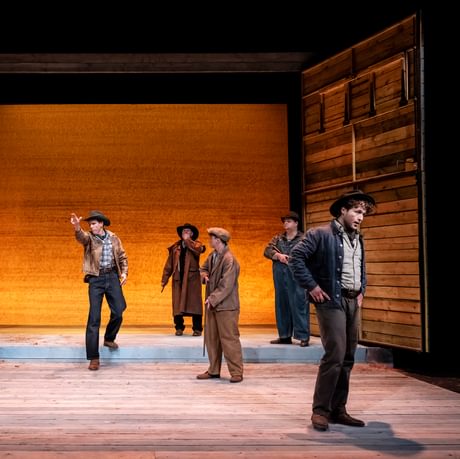 The actors are stood around the stage and one of them explains something.