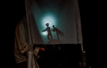 Image shows a white sheet with a light shining on it to show shadows of two figures chasing one another.