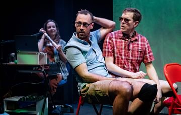 The actors sit on stage wearing glasses