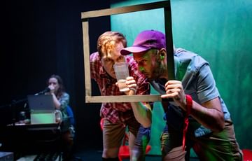 The actors are on stage holding a frame. They look through it intensely