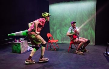 One actor is wearing a bike helmet, whilst the other is sat down shining a torch