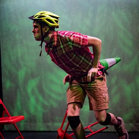 The actor wears a bike helmet on his head and a traffic cone on his back