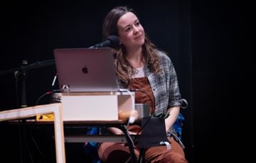 The actress sits behind a desk that has an opened laptop on it