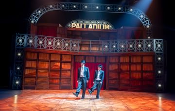 Two actors stand on stage doing a dance in the street