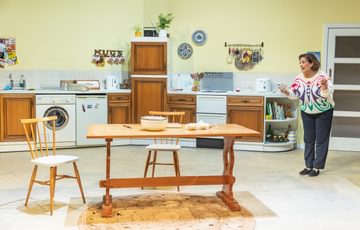 The actress is stood in the set of a kitchen. She is talking to herself.
