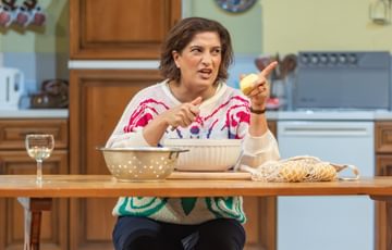 The actress sits behind a table speaking as she peels potatoes