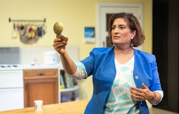 The actress stands on stage in a blue blazer holding and looking into a pocket mirror