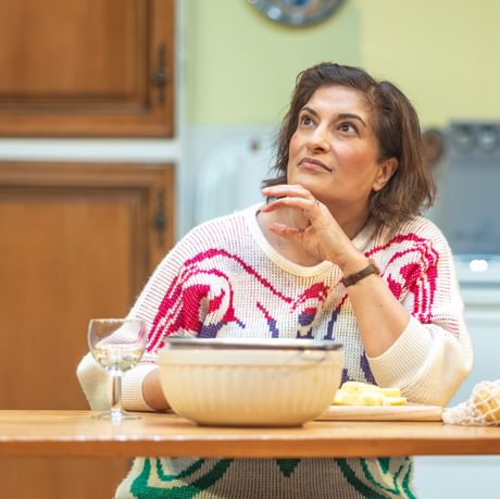 The actress sits behind a table looking up into the distance.