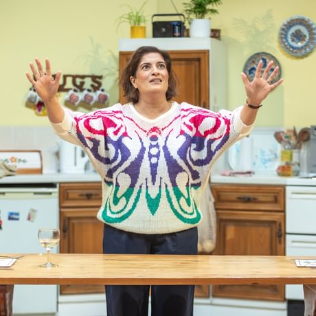 The actress stands in a kitchen set, behind a dining table
