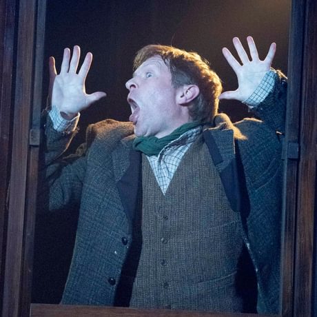 An actor is shown in frame with his hands and face pressed up against a window.