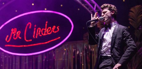 A man singing on a mike, with purple lighting in the background