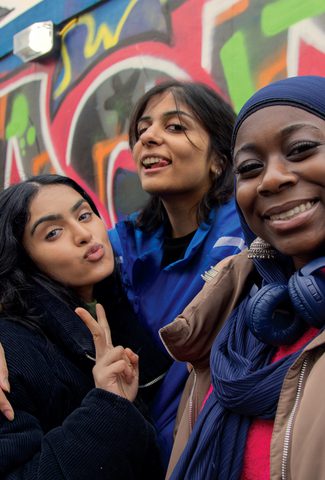 3 girls posing for a photo with a graffiti wall behind them