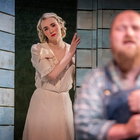 Emma Charlton, playing Curley's wife is stood in an entranceway onlooking Ben Wilson, playing Candy