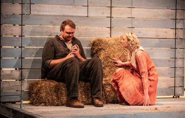 William Young who plays Lennie is sat on a bale of hay whilst Emma Charlton, who plays Curley's wife kneels beside him.