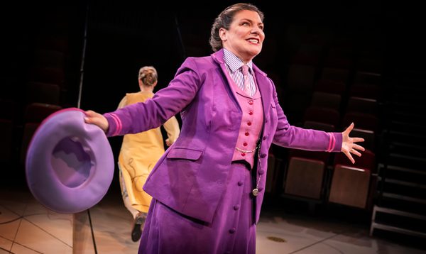 A woman wearing a purple suit doing jazz hands.