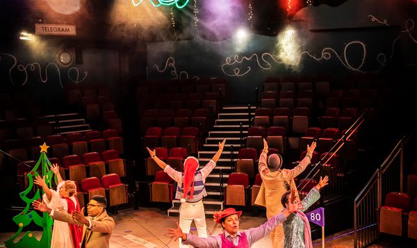 Full cast in a circle doing jazz hands with neon lights above their heads.