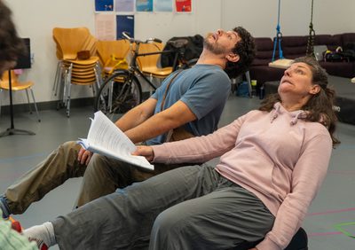 A man and a woman both sat leaning back on luggage trunks.