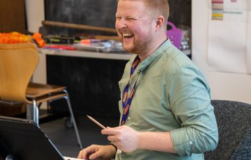 A man sat at a keyboard looking out and laughing.