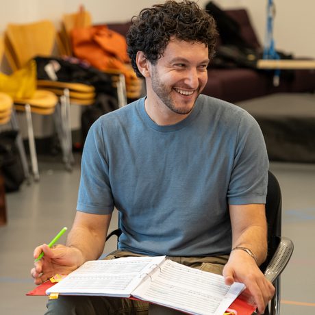 A man sat down with a folder open on his lap, looking to his side and laughing.