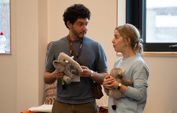 A man and a woman stood side by side looking at each other, both holding soft plush elephant teddies.