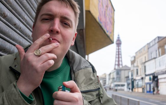Man lighting a cigarette with Blackpool tower behind him