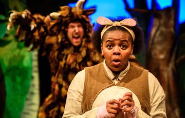 A woman dress as a mouse looking scared and Gruffalo growling in the background