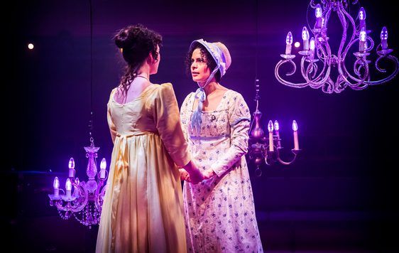 two women in regency clothing holding hands and looking intensely at each other