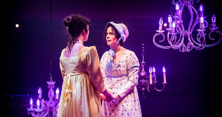 two women in regency clothing holding hands and looking intensely at each other