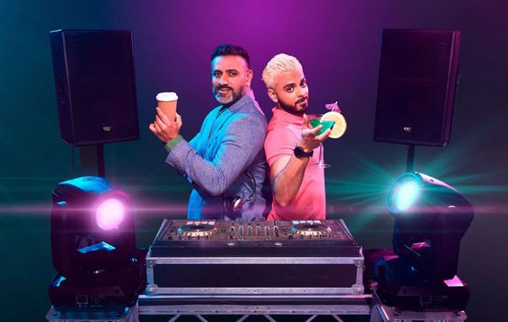 2 Asian men stood behind a DJ set. The older man has a coffee and the younger man has a cocktail.