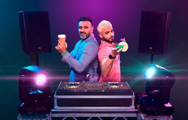 2 Asian men stood behind a DJ set. The older man has a coffee and the younger man has a cocktail.