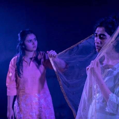 A girl wearing a sheer headscarf stood with a gentle expression. Next to her, another girl is holding one end of the scarf, her face reflecting a deep sense of sadness.