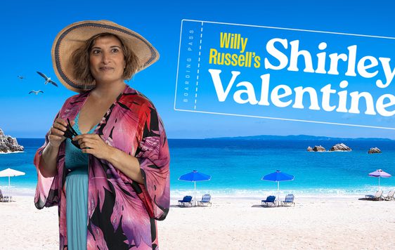 Actor Mina Anwar in a beach outfit with a Greek beach background