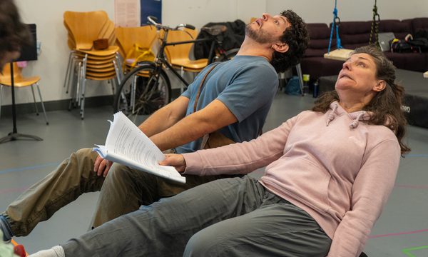 A man and a woman both sat leaning back on luggage trunks.