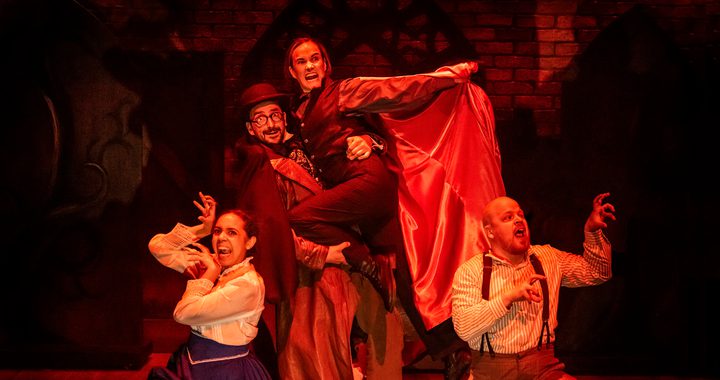 Image of 4 actors on stage with a red light, one of the actors is dressed as Dracula