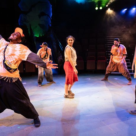 A woman surrounded by four people in orange costumes. With blue and yellow lights in the background.