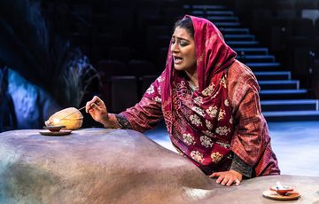 A woman in a traditional Indian costume lighting a candle with a match on a rock with blue lights in the background.