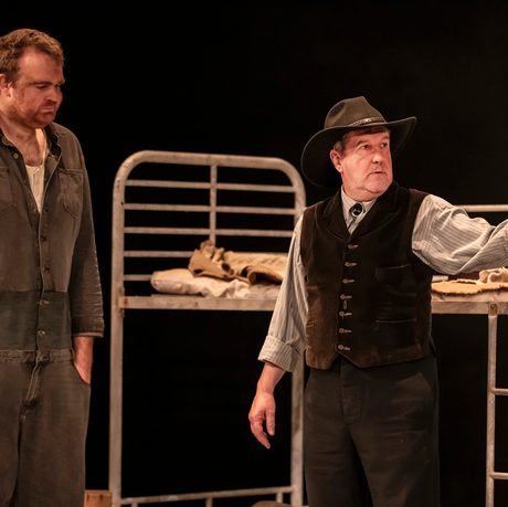 William Young playing Lennie stands with his hands in his pockets as John Elkington, playing 'The Boss' stands and points into the distance