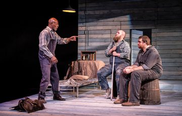 Jeff Alexander who plays crooks is stood up pointing at Ben Wilson, who plays Candy, and William Young, who plays Lennie.