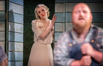 An actress is shown holding onto a wall as she looks at another actor further upstage