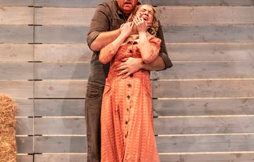 William Young who plays Lenny is holding Emma Charlton who plays Curley's wife by the mouth.