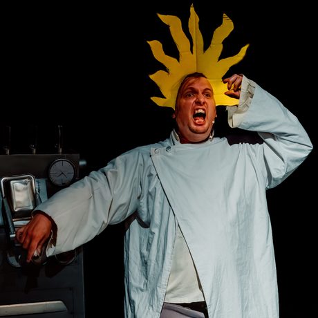An actor is shown wearing a flame headband whilst screaming in a comedic way