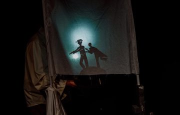Image shows a white sheet with a light shining on it to show shadows of two figures chasing one another.