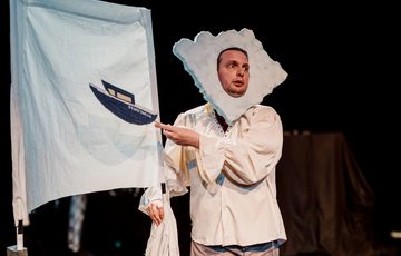 Actor is shown in front of a white sheet, holding an image of a boat.