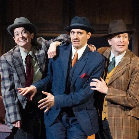Three actors stand on stage holding onto one another