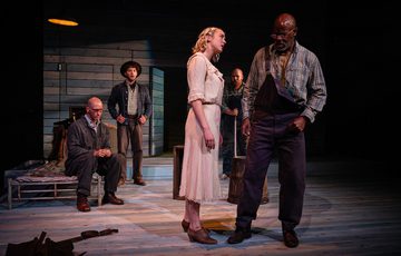 The actors are spread around the stage looking concerned and serious.