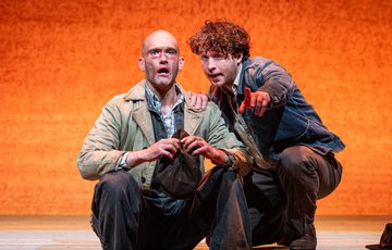 Luke Richards who plays Lennie, is sat on the floor whilst Liam King who plays George kneels beside him.