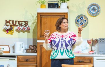 The actress stands up holding a wine glass as she points off into the distance
