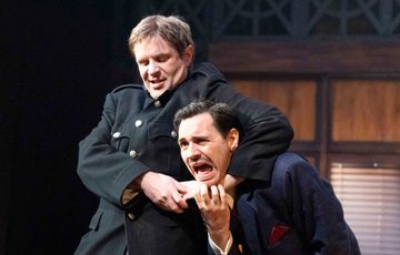 Two actors are shown. On has the other in headlock.